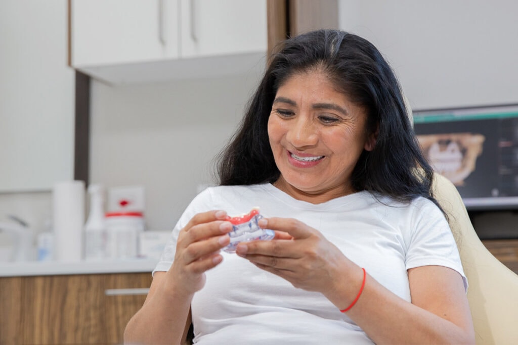 Full Mouth Dental Implant Patient Mercy Smiling At An All-On-X Model In Her Hands